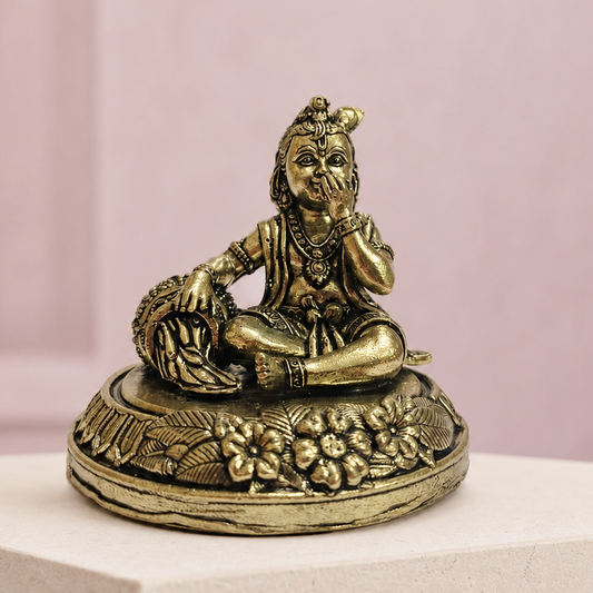 Bal Krishna Brass Idol with Butter Pot on an ivory platform with a soft mauve heritage backdrop