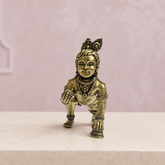 Crawling Bal Krishna Brass Idol on an ivory platform with a soft mauve heritage backdrop