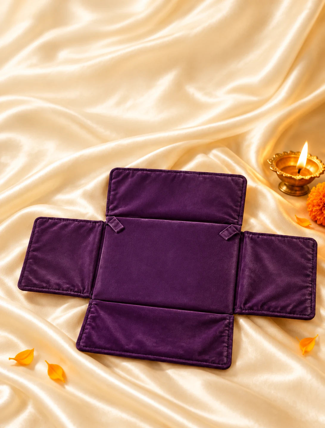 A brinjal jewellery gift pouch on ivory silk beside a glowing Diwali lamp